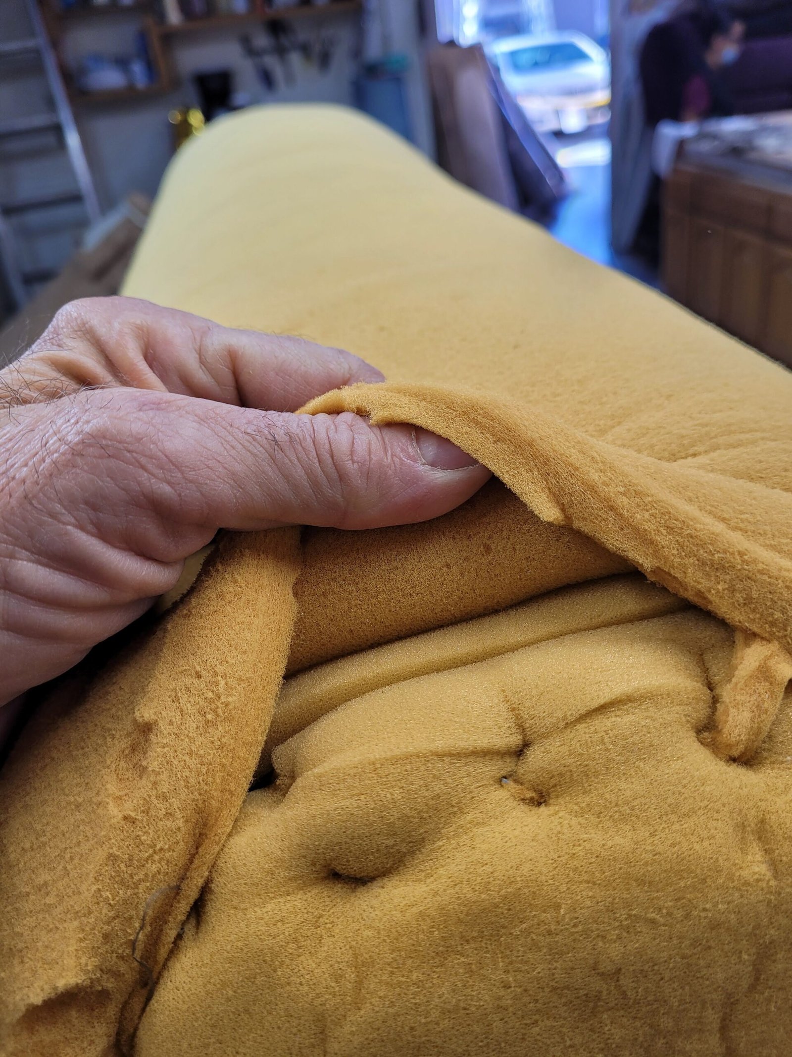 Hand lifting a foam layer on a rolled sofa arm during rebuilding