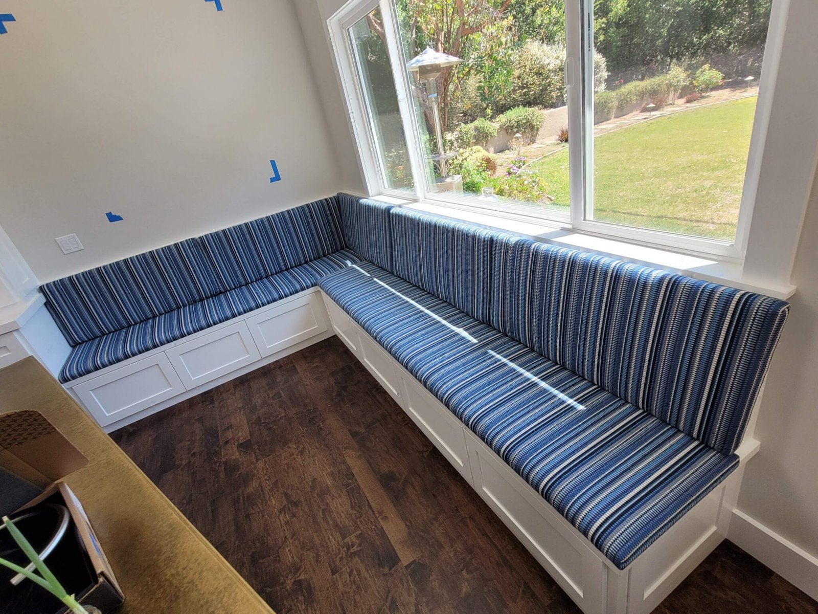 Built-in kitchen nook banquette upholstered in blue and white striped fabric beside a sunlit window