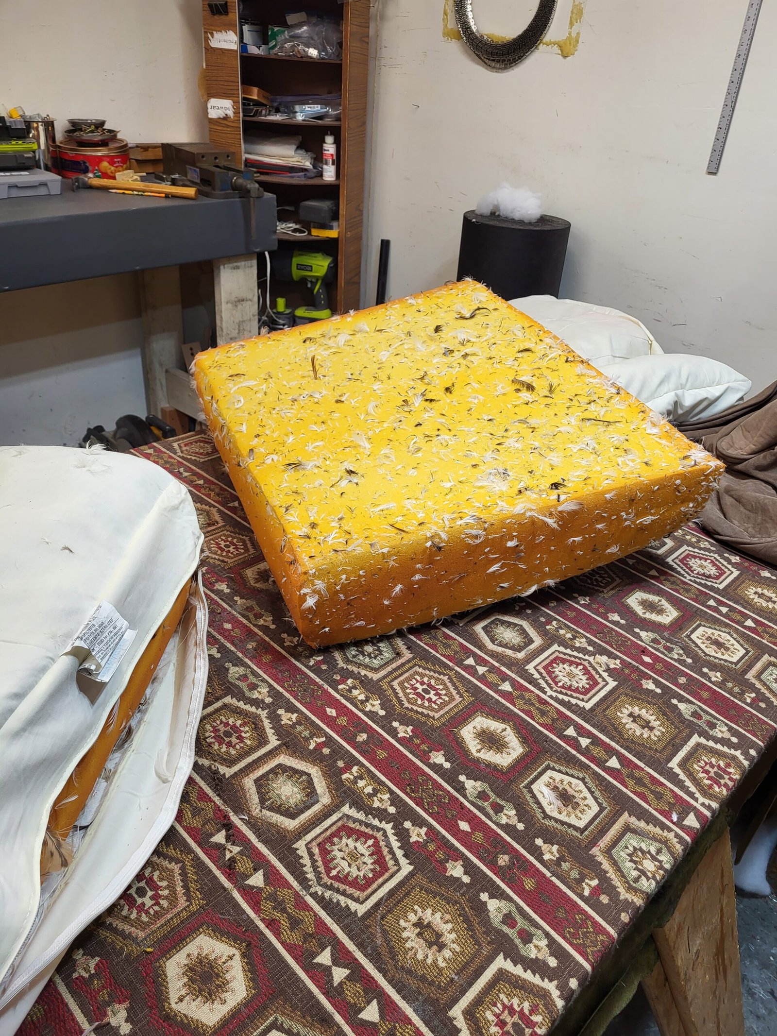 Degraded yellow foam cushion covered in feather debris on a workshop bench