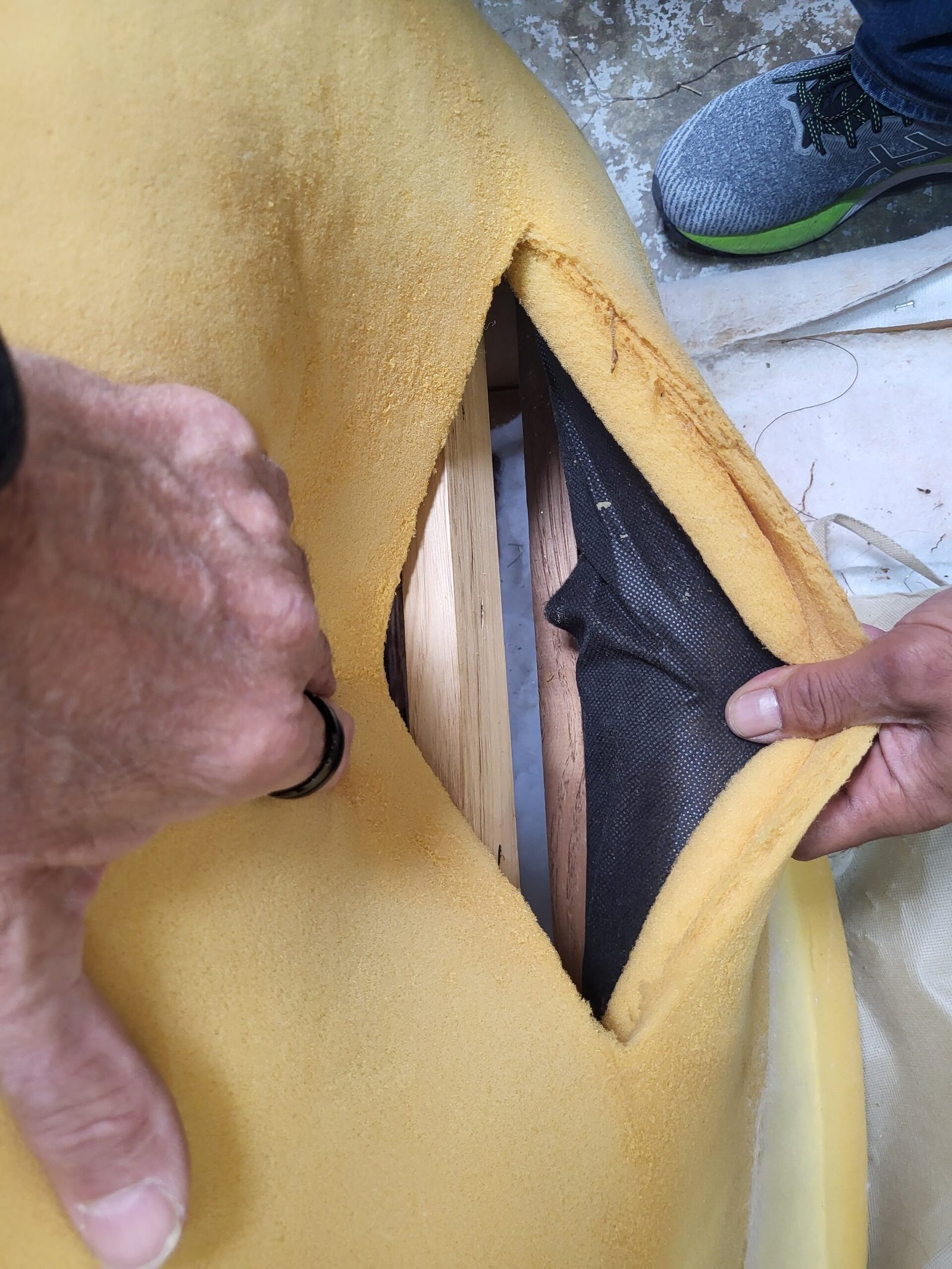 Hands peeling foam back from a chair to expose the hardwood frame beneath