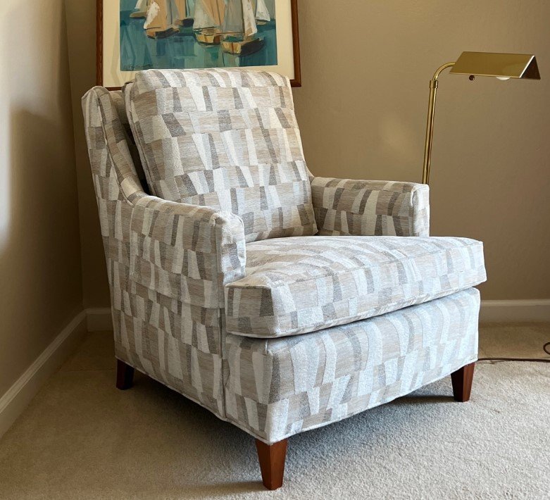 Wing chair reupholstered in a geometric grey and cream fabric beside a brass lamp