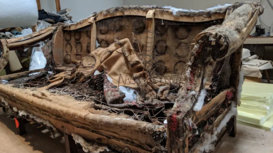 Sofa stripped back to its bare hardwood frame, showing exposed coil springs and original burlap before rebuilding
